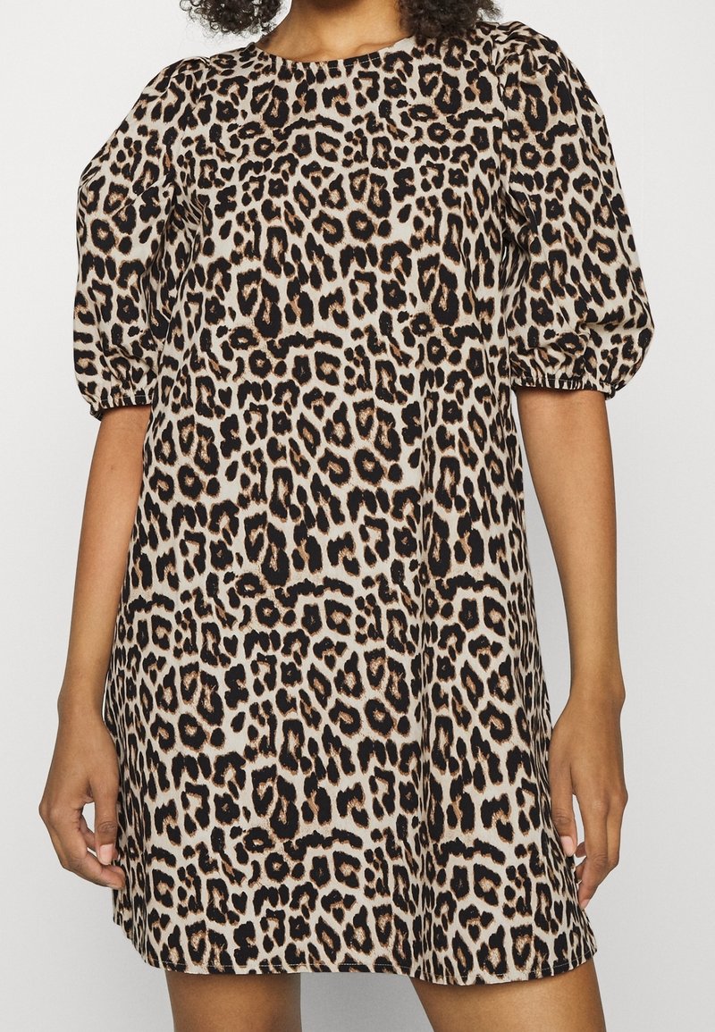 Femme portant une robe courte à manches courtes, longueur genou, avec un imprimé léopard beige, noir et marron et des manches bouffantes.