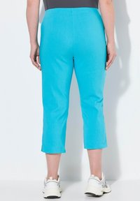 Pantalons turquoise raccourcis en tissu léger avec une texture lisse, dotés d'une taille plate et de fentes sur le bas.