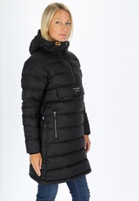 Svart pufferjacka med hög krage, framficka med dragkedja och tryckknappar längs sidan. Har en vadderad struktur och huva.