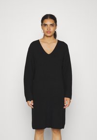 Robe tricotée noire avec un décolleté en V profond, des manches longues, une coupe décontractée et une longueur mi-mollet. Le tissu texturé ajoute un intérêt visuel.