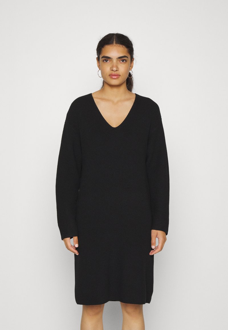 Robe tricotée noire avec un décolleté en V profond, des manches longues, une coupe décontractée et une longueur mi-mollet. Le tissu texturé ajoute un intérêt visuel.
