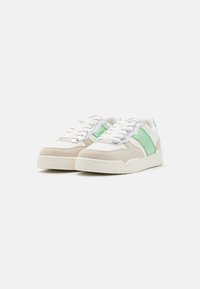 Baskets avec un dessus en suede beige, des accents en suede vert et des détails métalliques argentés ; semelle en caoutchouc texturée blanche ; fermeture à lacets classique.