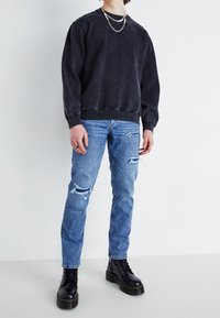 Mikina v antracitové šedé barvě s žebrovaným lemem, světle modré džíny s roztrhanými koleny a černé šněrovací boty s masivní podešví.