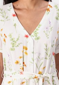 Blommig klänning i lätt tyg med v-ringning, korta ärmar, knäppning fram och knyt i midjan. Färgerna inkluderar vitt, grönt, rosa och gult.