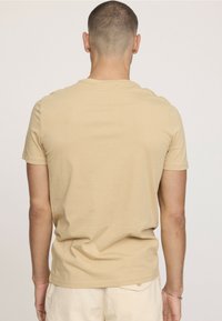 T-shirt en coton beige à manches courtes, col rond et coupe décontractée. Texture lisse, coutures minimales et sans accents ou motifs notables.