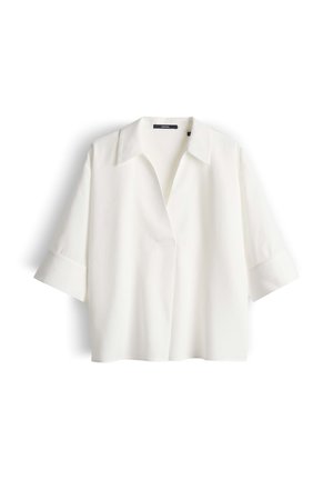Blusa bianca dalla vestibilità ampia con maniche larghe 3/4, colletto aperto e senza bottoni visibili, mostrata su uno sfondo bianco.