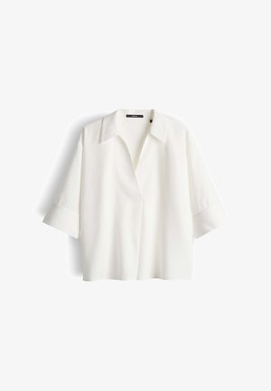 Blouse blanche, ample, avec des manches larges aux trois quarts, col ouvert et sans boutons visibles, posée sur un fond blanc.