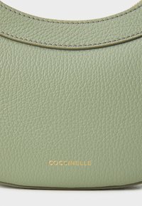 Green textured leather bag with a curved top. Features embossed gold branding on the front, with seamless stitching along the edges.