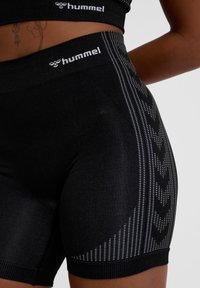 Zwarte sportshorts met een gestructureerde tailleband, met een geometrisch patroon in wit en zwart aan de zijkant, gemaakt van rekbaar materiaal.