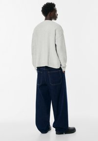 Maglione lavorato a maglia grigio chiaro con spalle scese e orlo a costine. Jeans a gamba larga blu navy con cuciture visibili e tasche posteriori, abbinati a stivali neri.