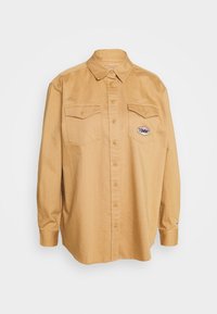 Camicia a maniche lunghe beige con bottoni frontali, due tasche sul petto e logo ricamato "TOMMY" sulla tasca sinistra. Tessuto leggero.