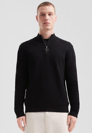 Black knitted pullover with a high collar and half-zip closure. Features ribbed texture and fitted cuffs.