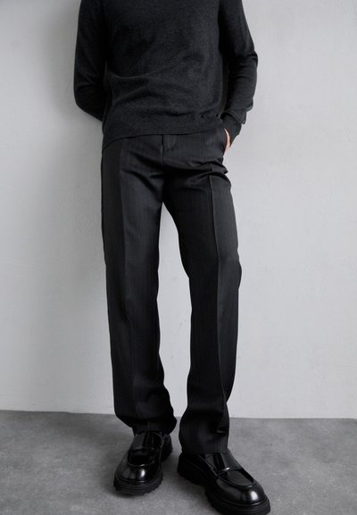 Sort uldblandingsstrik med rund hals, parret med charcoal stribede bukser. Kraftige sorte loafers med en glat overflade.