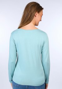 Helles blaues Langarmhemd mit rundem Ausschnitt und gerippten Details am Kragen; weicher Stoff mit glatter Textur.