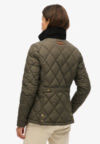 Gequiltede groene jas met een zwarte corduroy kraag, gouden knoopaccenten en een getailleerde taille, die een modern, gestructureerd ontwerp laat zien.