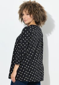Zwarte tuniek met kleine witte bloemenpatronen, lange mouwen, ronde halslijn en een iets relaxed fit. Zachte stof met een gladde textuur.