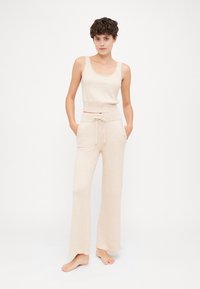 Ανοιχτό μπεζ αμάνικο τοπ και αντίστοιχες φαρδιές παντελόνες φτιαγμένες από μαλακό, υφασματισμένο υλικό με ρυθμιζόμενη ζώνη στη μέση.