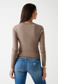 Pull en brun ajusté à manches longues, avec un col et des poignets côtelés, associé à un jean en denim bleu avec une étiquette logo sur la poche arrière.