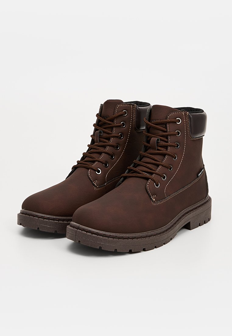 Stivali alla caviglia in pelle marrone con suole in gomma nera robuste, punta rotonda, occhielli metallici e design con lacci. Presentano un colletto imbottito e cuciture a contrasto.