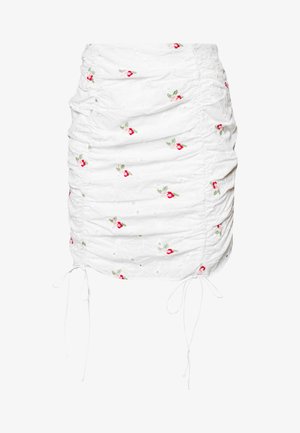 Mini-jupe blanche froncée avec une petite broderie florale rouge et rose et des cordons réglables des deux côtés.