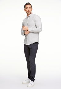 Lichtgrijs shirt met lange mouwen, met een kraag met knopen en een borstzak. Gewikkeld met marineblauwe broek en witte sneakers. Eenvoudige textuur over het geheel.