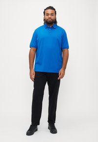 Blå poloshirt med korte ærmer, sorte bukser og sorte sneakers. Skjorten har en krave og et lille logo på brystet.