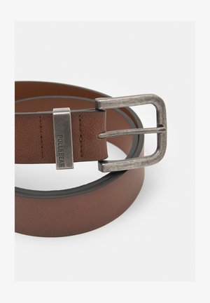 Barna műbőr öv ezüst színű fém csattal. Texturált felülettel rendelkezik és téglalap alakú csattal, amelyen a márka logója található.