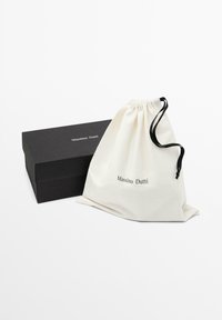 Cotton drawstring bag in off-white with "Massimo Dutti" logo, next to a black rectangular box with a matte finish.