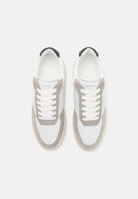 White and gray leather sneakers featuring perforated detailing, a rounded toe, flat laces, and a contrasting black heel tab.