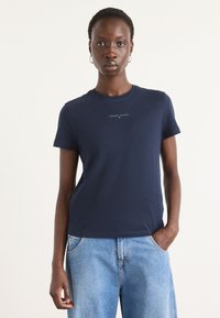 T-shirt in cotone navy con maniche corte, scollatura a girocollo e stampa del logo sul petto. Abbinato a pantaloni in denim blu chiaro.