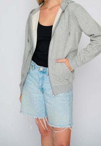 Šedá mikina na zip s fleecovou podšívkou, nastavitelnými šňůrkami a předními kapsami, spárovaná s světle modrými ošoupanými šortkami.