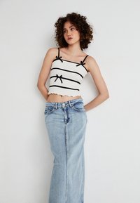 White cropped top with black horizontal stripes and bow accents; paired with light blue, high-waisted denim maxi skirt featuring a front slit.