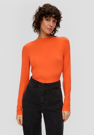 Langärmliges, tailliertes Oberteil aus leuchtend orangefarbenem Stoff, kombiniert mit hoch taillierten schwarzen Hosen mit doppeltem Knopfverschluss und strukturiertem Finish.