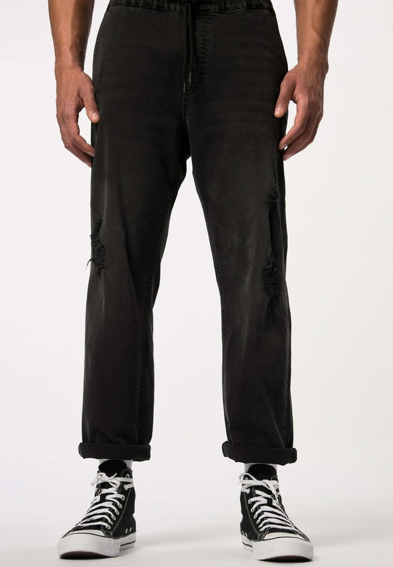 Pantalones de mezclilla negros con un corte relajado, que presentan detalles desgastados en las rodillas, una cinturilla con cordón y puños enrollados, combinados con zapatillas altas.