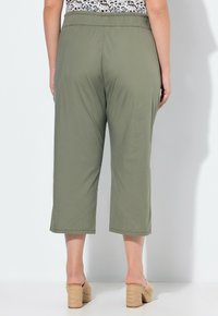 Olijfgroene cropped broeken met een elastische tailleband, voorzien van een soepele textuur en wijde pijpen, gecombineerd met lichte block-heel sandalen.