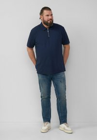 Granatowa koszulka polo z zamkiem przy kołnierzyku, w połączeniu z jasnoniebieskimi dżinsami i beżowymi trampkami. Luźny krój z krótkimi rękawami i prostym wzorem.