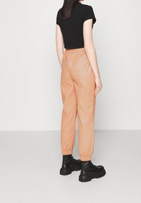 Pfirsichfarbene synthetische Hosen mit elastischen Bündchen, seitlichen Taschen und einer glatten Textur, kombiniert mit schwarzen Schnürstiefeln.