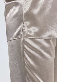 Metallisches silbernes Gewebe mit glatter Textur verfügt über einen seitlichen Schlitz, der ein glänzendes Finish und ein elegantes Design zur Schau stellt.