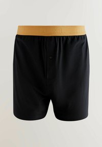 Melni kokvilnas bokseršorti ar dzeltenu jostu, kas rotāta ar teksturētu dizainu un vienu pogu priekšpusē.