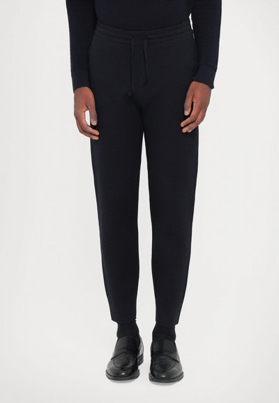 Pantalones jogger en navy con cintura ajustable, diseño tapered y tejido suave; combinados con zapatos de cuero negros.