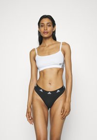 Bílý sportovní podprsenka s tenkými ramínky a černými dekorativními pruhy. Černé bikiny s bílým logem Adidas a obvodem kolem pasu.