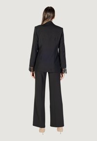 Completo strutturato nero con giacca su misura e pantaloni larghi. La giacca presenta dettagli in pizzo sui polsini per un tocco di eleganza in più.