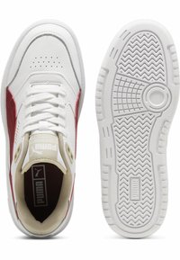 Baskets blanches de sport avec des accents rouges, tige en cuir texturé, fermeture à lacets classique, et semelle en caoutchouc avec un motif de bande en zigzag.