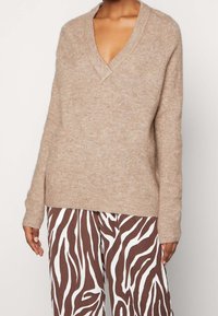 Beige V-Ausschnitt-Pullover aus weichem Stoff mit langen Ärmeln. Kombiniert mit braun-weißen, zebra-gemusterten Hosen im lässigen Schnitt.