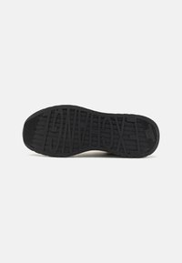 Svart såle med teksturert mønster og store, stiliserte bokstaver som danner "XAGON" over bunnen.