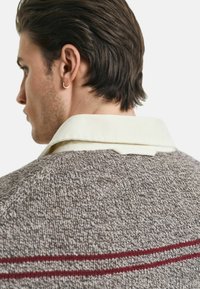 Pull en laine marron avec un tricot fin, doté d'un col crème et de deux fines rayures rouges sur le dos.