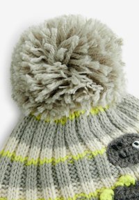 Bonnet en tricot avec un pompon en peluche gris clair, motif rayé en gris, crème et jaune néon, et un appliqué d'animal texturé gris.