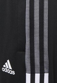 Black athletic jacket featuring a smooth texture, three white vertical stripes with a grid pattern, and a white logo on the left side.