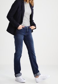 Mörkblå jeans med uppvikta benslut, kombinerat med en figurformad grå ribbad tröja och en svart kavaj. Vita sneakers fulländar outfiten.