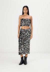Conjunto de dos piezas en negro y plateado con lentejuelas que incluye un top sin tirantes y una falda de longitud media, combinado con botas negras hasta el tobillo. Textura suave.